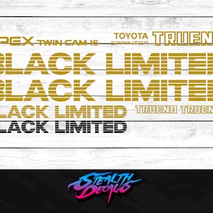 May include: Gold and black vinyl decal stickers with the text "APEX TWIN-CAM 16 TOYOTA SPRINTER TRUENO BLACK LIMITED" repeated four times. The text is in a retro style font with a striped pattern. The stickers are on a white wood background.