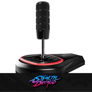 Peut inclure: Pommeau de levier de vitesses noir avec une poignée texturée, monté sur une base noire avec un accent rouge. La base a un motif de changement de vitesse. Le logo "Stealth Decals" est en bas.