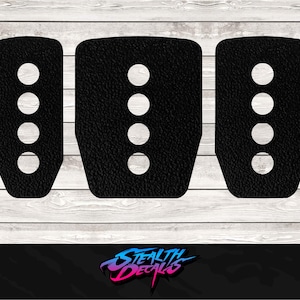 Puede incluir: Tres cubiertas de pedal negras con recortes circulares blancos. Las cubiertas tienen una superficie texturizada y están dispuestas sobre un fondo claro de vetas de madera. El logotipo "Stealth Decals" está en la parte inferior.
