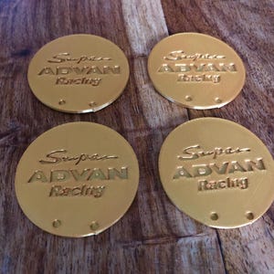 以下が含まれることがあります： 「Supra ADVAN Racing」と刻まれた、金色の丸い金属製のコースターが4つあります。