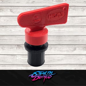 May include: A red and black bottle stopper with the word "NISMO" on the top. The stopper has a textured handle and a cylindrical base. The product is designed to fit into a bottle.