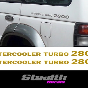 May include: A white car with a silver "INTERCOOLER TURBO 2800" decal on the side. The decal is a popular modification for car enthusiasts.