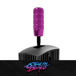 May include: A purple aluminum gear shift knob with a black base. The knob has a ribbed design and is mounted on a black gear shift lever.