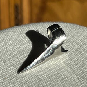 May include: A silver ring with a pointed, sharp design. The ring is made of metal and has a unique, modern style.
