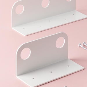 Può includere: Due staffe per mensole in metallo bianco con angoli arrotondati e tre fori circolari. Ogni staffa ha una base piatta con fori preforati per il montaggio. Sono incluse tre viti bianche.