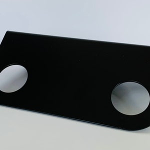 Może przedstawiać: Czarny metalowy wspornik z dwoma okrągłymi otworami. Wspornik jest pochylony i ma gładką, płaską powierzchnię.