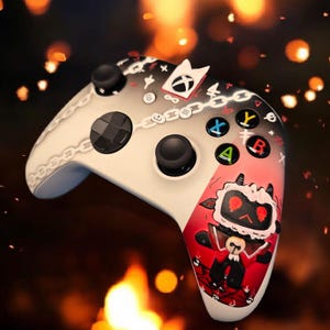 May include: White and black video game controller with a cartoon character design. The controller has black joysticks, colored buttons, and a chain design. The right side features a red and white cartoon character.