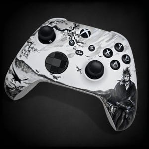 May include: White Xbox controller with a custom Japanese-style design in black and white. The artwork depicts a samurai, birds, and a landscape. The controller has black buttons and directional pads.