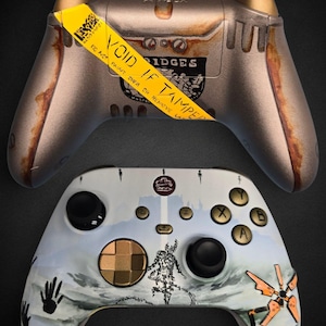 May include: Two custom Xbox controllers. The top controller has a metallic finish with rust-like accents and a yellow "VOID IF TAMPERED" sticker. The bottom controller is white with a painted landscape design, black buttons, and gold accents.