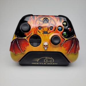 May include: Custom Xbox controller with a fiery design. The controller features a pentagram, skull, and dragon wing accents. The base has the text "BEETLE DASH". The color scheme includes black, orange, and red.