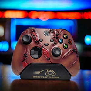 May include: A custom Xbox controller with a brown and red design, featuring a stitched pattern and a black base with the text "BEETLE DASH". The controller has black buttons and a directional pad, and is designed for gaming.