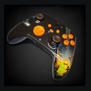 Puede incluir: Mando de videojuegos negro personalizado con un diseño de cielo estrellado y botones naranjas. El mando presenta una escena de paisaje pintada con una fogata y árboles.
