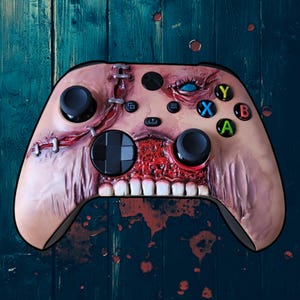 Può includere: Un controller per videogiochi personalizzato a tema zombie. Il controller presenta un esterno color carne con ferite esposte e cucite, una bocca spalancata e un singolo occhio blu. I pulsanti sono di vari colori.