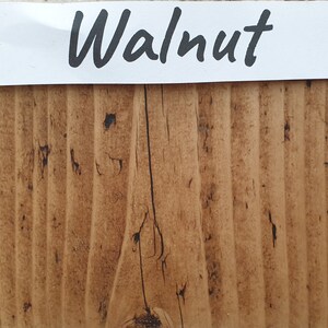 May include: A close-up of a wood sample stained in a walnut color. The wood has a natural grain pattern and a slightly rough texture.