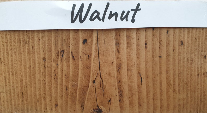May include: A close-up of a wood sample stained in a walnut color. The wood has a natural grain pattern and a slightly rough texture.