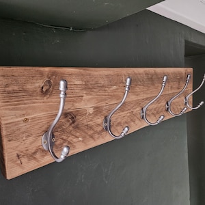 May include: A rustic wooden coat rack with five silver hooks. The rack is made of reclaimed wood and has a natural, weathered finish.