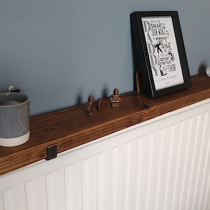 May include: A rustic wooden shelf mounted above a white radiator. The shelf is decorated with a gray mug, a framed print with the text "Daddy", and two small figurines.
