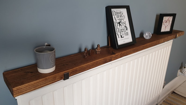 May include: A rustic wooden shelf mounted above a white radiator. The shelf is decorated with a gray mug, a framed print with the text "Daddy", and two small figurines.