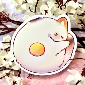 May include: A white cat curled up in a circle, resembling a fried egg with a bright yellow yolk. The cat's tail is curled around its body, and its eyes are closed.
