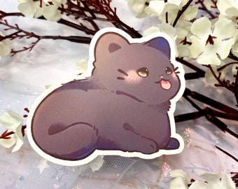 May include: A sticker of a cartoon gray cat with a pink blush on its cheeks, sticking its tongue out. The cat is sitting on a white background.