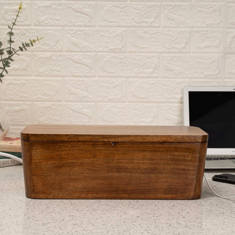 a wooden box placed on a white speckled countertop, with a laptop and a plant in the background.