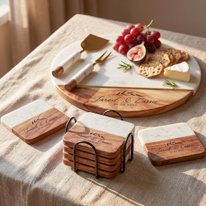 a wooden serving platter with a variety of food items, including grapes, cheese, crackers, and a knife, arranged on a table. The platter also has coasters with the names 'Jared & Cassie' printed on them.