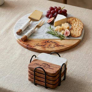 A marble serving platter with a variety of food items, including grapes, cheese, crackers, and a rosemary sprig, is displayed on a table. The platter also has a set of coasters with the names 'Jared & Cassie' printed on them.