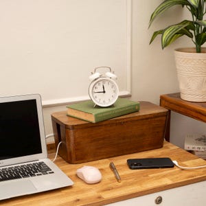 a wooden desk with a laptop, a white alarm clock, a green book, a black phone, a white mouse, and a potted plant.
