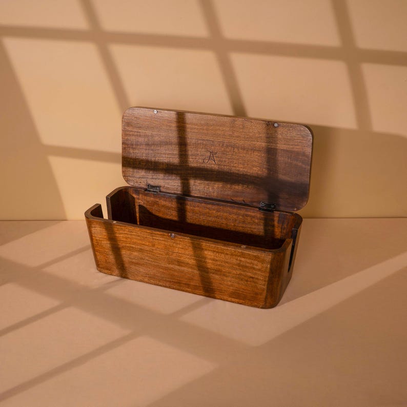 A wooden box with a lid, sitting on a beige surface and casting shadows on the wall behind it.