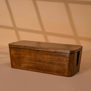 A wooden cable box or cable organizer sits on a light-colored surface against a beige background.