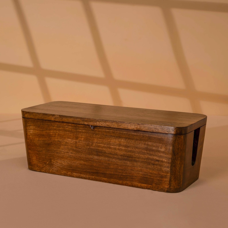 A wooden cable box or cable organizer sits on a light-colored surface against a beige background.
