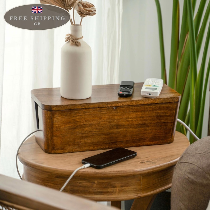 a wooden table with a vase of flowers, a wooden box, and a smartphone charging on the table.