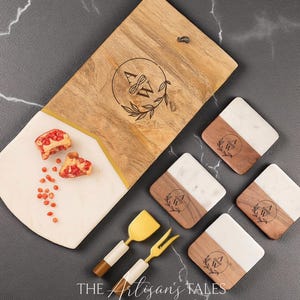 May include: A rectangular wooden and white marble serving board with a gold accent line, four square marble and wood coasters, a gold cheese spreader, and a gold cheese fork. Each piece features a laser-engraved circular logo with the letters A&W.