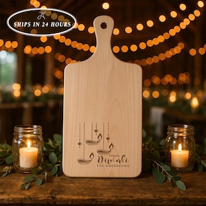 May include: A light-colored wooden serving board with a handle and a hole for hanging. The board features an engraved design of three hanging diya lamps and the text "happy Diwali THE ANDERSONS" centered near the bottom of the board.