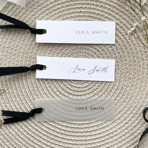 May include: Three place cards with the name "Luca Smith" written in different styles. The top card is printed in a simple font, the middle card is written in cursive, and the bottom card is printed on a translucent material with a wavy texture.