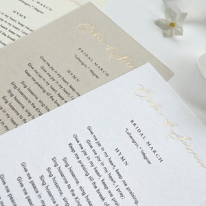 May include: Three cards with the text "Order of Service" in gold script. Each card has the title "Bridal March" and the text "Lohengrin, Wagner" in gold script. The cards also include the text "Hymn" and the lyrics to the song "Give me joy in my heart, keep me praising" in black text.