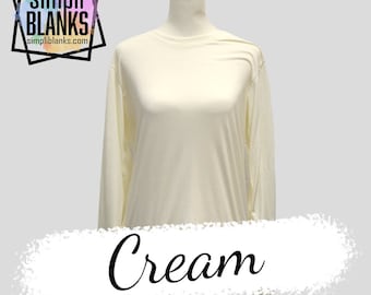 May include: A cream colored long-sleeved t-shirt on a mannequin. The shirt is made of a soft, stretchy fabric. The text "simpli BLANKS" and "simpliblanks.com" is printed on a black square in the top left corner of the image. The word "Cream" is written in a decorative font below the shirt.
