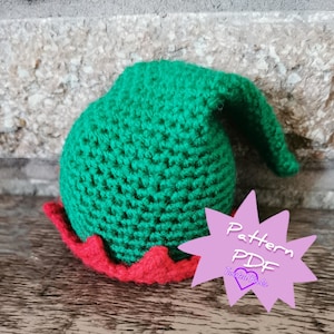 Peut inclure: Un chapeau d'elfe au crochet vert fait à la main avec un bord festonné rouge. Le chapeau est fait d'un fil texturé et a une pointe. Un graphique en forme d'étoile rose avec le texte "Pattern PDF Twisted Hooks" est dans l'image.