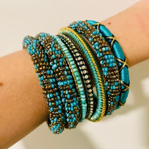 Puede incluir: Una pila de pulseras de cuentas turquesa y doradas con algunos detalles de pedrería.