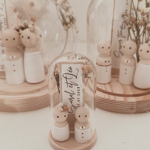 以下が含まれることがあります： ガラスのドームの中に、花嫁と新郎の小さな木製の置物が2体入っています。ドームの中にはドライフラワーと「Jared et Dieu 17.07.2023」と書かれた小さなカードが入っています。