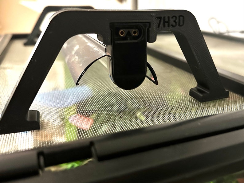 Puede incluir: Un accesorio de l&aacute;mpara de pl&aacute;stico negro con una pantalla de metal y un cable de alimentaci&oacute;n. El accesorio est&aacute; etiquetado como "7H3D".