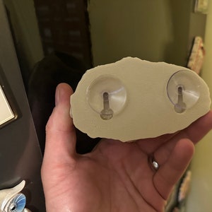 May include: A beige, rock-shaped wall mount with two clear suction cups on the back.