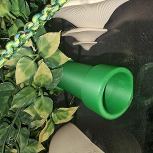 May include: A green plastic tube with a smooth, rounded surface. The tube is attached to a wall or surface.