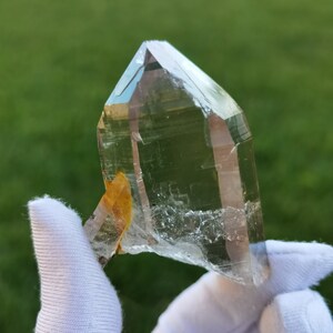 May include: A large, clear quartz crystal with a natural, raw edge. The crystal is held in a white cloth and has a slight yellow tint.