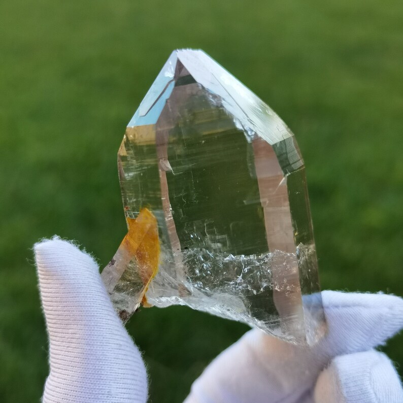 May include: A large, clear quartz crystal with a natural, raw edge. The crystal is held in a white cloth and has a slight yellow tint.