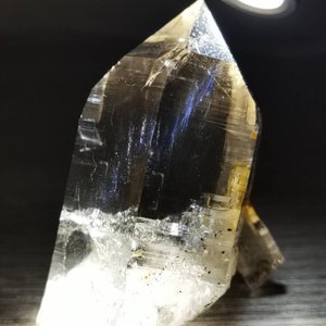 May include: A large, clear quartz crystal with a pointed tip and a flat base. The crystal is illuminated by a light source, highlighting its internal structure and facets.