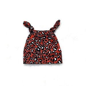 Könnte beinhalten: Eine rote und schwarze Baby-Mütze mit Leopardenmuster und Knoten.