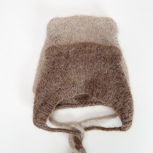 Peut inclure: Un bonnet bébé en tricot marron et beige avec des oreilles et une ficelle.