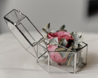 May include: A glass box with a silver frame holds a pink rose and green leaves. The box is open and the lid is lying on its side.