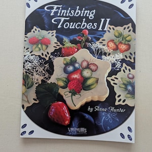 May include: A book cover titled "Finishing Touches II" by Anne Hunter. The cover features a dark blue background with painted strawberries, blueberries, and other berries on decorative plates. The Viking brand logo is visible.
